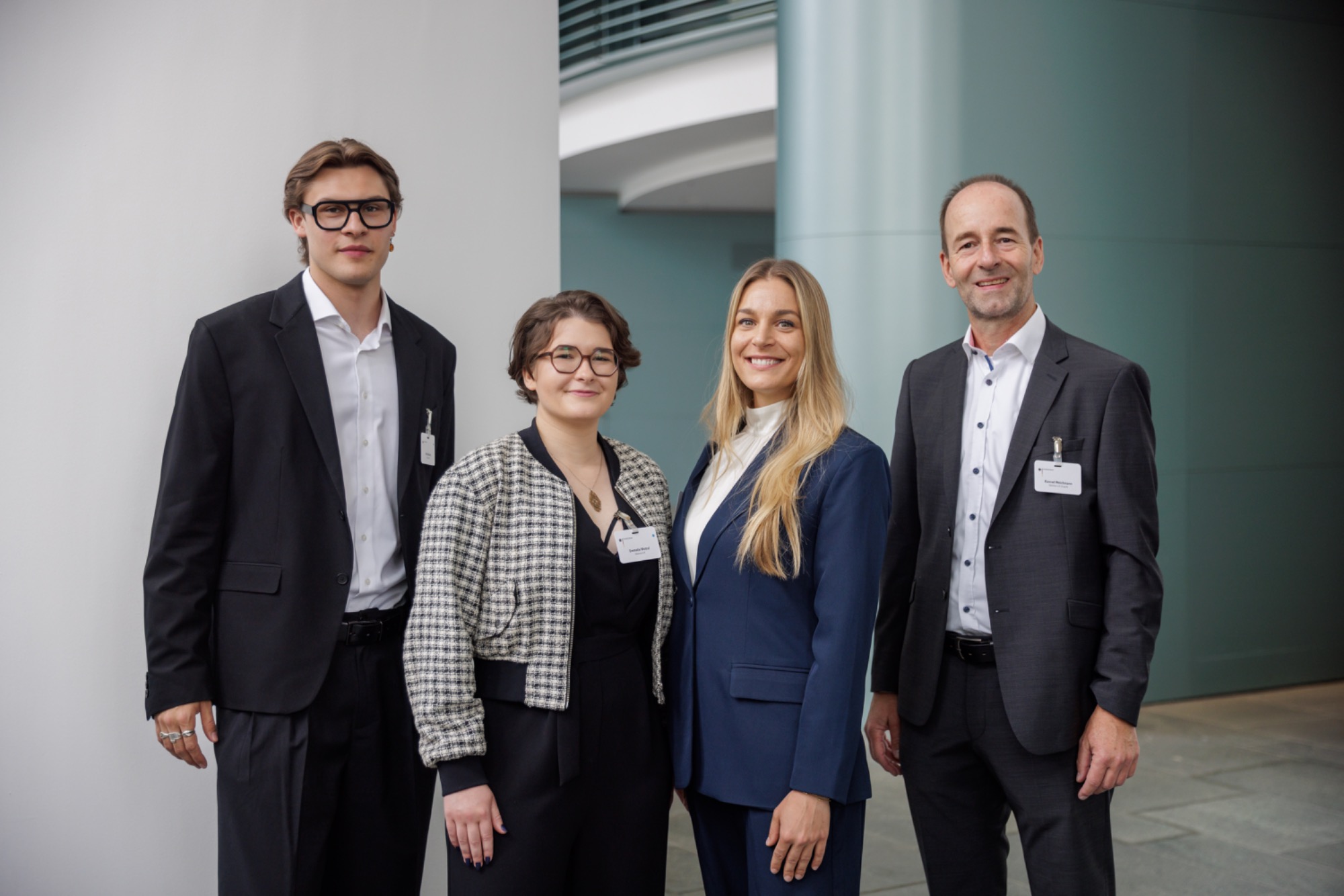 Gemeinsam im startsocial-Beratungsstipendium: Nils, Emmelie und unsere Coaches Lisa Jacob und Konrad Weichmann Vier Personen in formeller Kleidung stehen in einem modernen Innenraum.