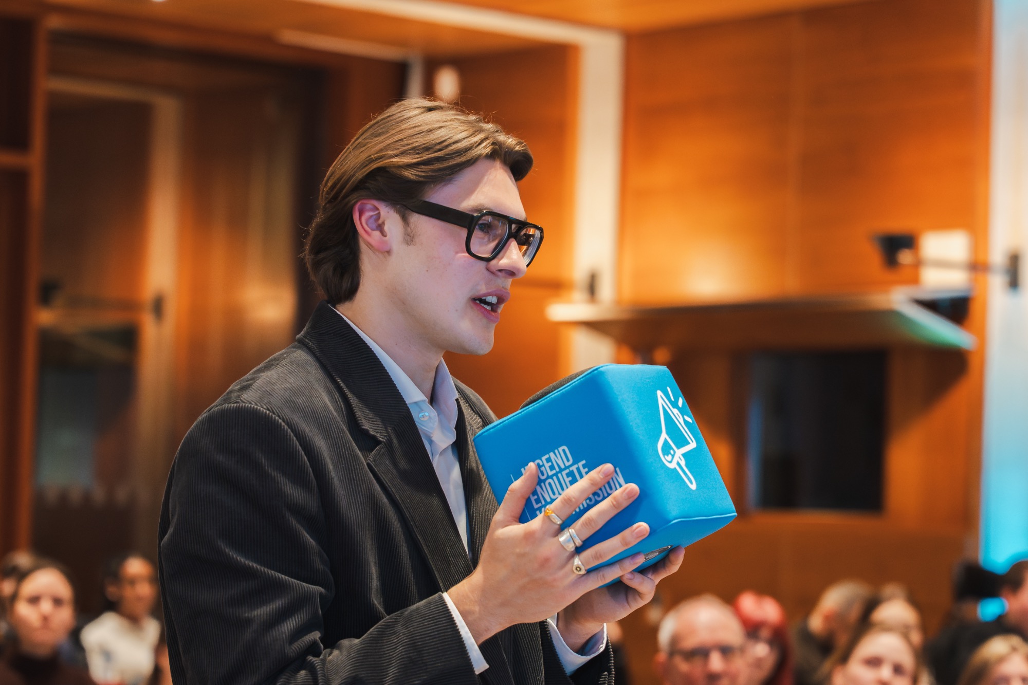 Junge Stimmen im Bildungsdialog: Nils stellt eine Frage zum Policy Paper zur Bildungsgerechtigkeit Mann mit Brille präsentiert einen blauen Würfel bei einer Veranstaltung.