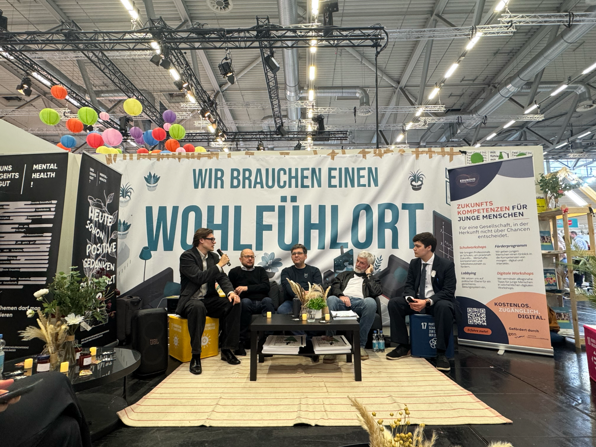 Gemeinsam mit der Bundesschülerkonferenz auf der Didacta 2026: Bildungsgerechtigkeit aus Sicht junger Menschen Fünf Personen sitzen an einem Tisch vor einem Banner mit dem Text "WIR BRAUCHEN EINEN WOHLFÜHLORT".